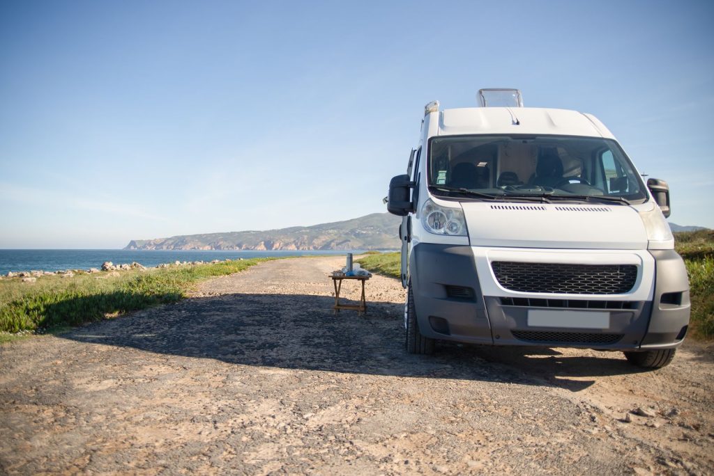 Van aménagé garé au bord d’une route côtière, la mer en contrebas