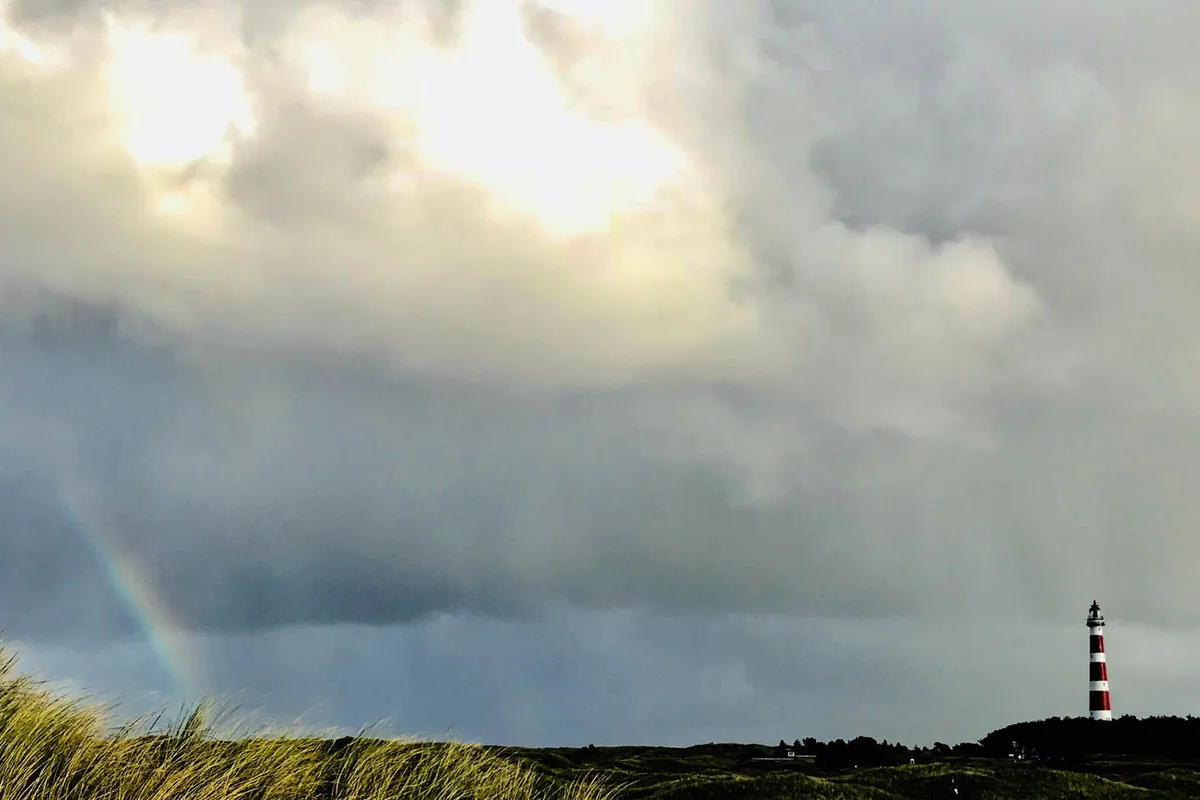 Phare dans les herbes sous un ciel d'orage et un arc-en-ciel